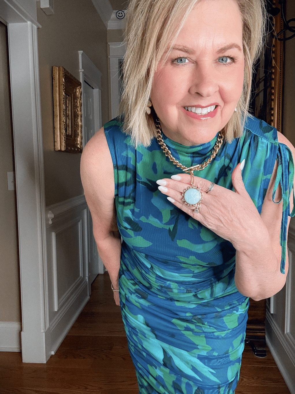 Tania Stephens is wearing a sleeveless maxi spring wedding guest dress with a blue necklace